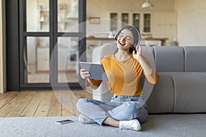 Relaxed indian lady in headphones listening music on digital tablet at home