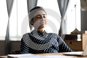 Relaxed indian young woman rest sit at desk eyes closed photo
