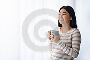 Relaxed Korean Female Drinking Coffee While Standing Near Window At Home
