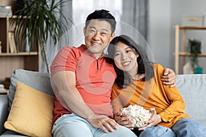 Relaxed korean spouses sitting on sofa, watching movie together