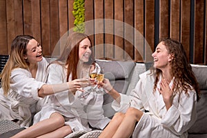 Relaxed ladies enjoy drinking champagne at spa. Three beautiful women wearing bathrobes having cool resting, holidays