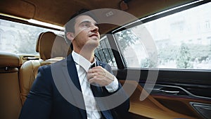 Relaxed male ceo sitting in comfortable car afterwork. Business man fixing tie