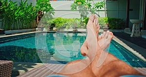 Relaxed man on holiday vacation near blue swimming pool water. Boy bare feet on the background. Brutal male legs with