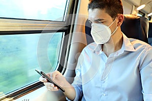 Relaxed man with KN95 FFP2 face mask using smart phone app. Train passenger with protective mask  texting on mobile phone. Travel