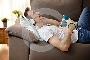 Relaxed man lying on a sofa with headphones listening music