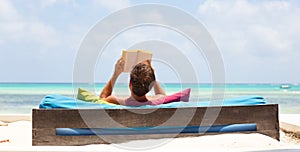 Relaxed man reading book in luxury lounger enjoying summer vacations on beautiful beach.