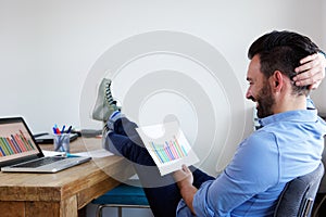 Relaxed man reading business graphs at office