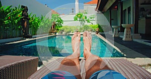 Relaxed man resting on lounger on holiday vacation near blue swimming pool water. Boy bare feet on the background