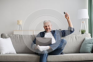 Relaxed man sitting on couch with laptop, turn on AC photo