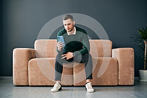 Relaxed man sitting on couch using hsi mobile phone
