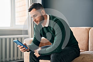 Relaxed man sitting on couch using hsi mobile smart phone