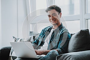 Relaxed man smiling while sitting on the sofa with laptop