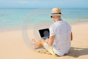 Relaxed man working with laptop on the beach