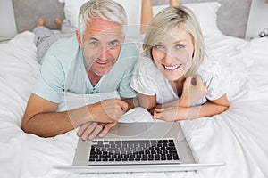 Relaxed mature couple using laptop in bed