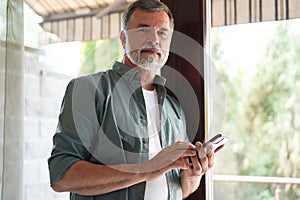Relaxed mature man at home standing by the window.