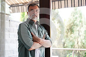 Relaxed mature man at home standing by the window.