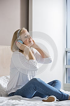 Relaxed mid adult woman enjoying music on headphones in bedroom