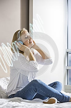 Relaxed mid adult woman listening music through headphones on bed