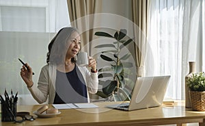 Relaxed middle aged woman sitting in front of laptop computer in living room and drinking hot coffee