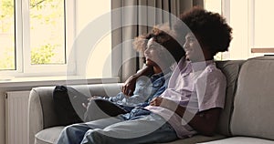 Relaxed millennial African family couple cuddle on sofa watch TV