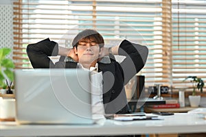 Relaxed millennial businessman sitting back in office chair with closed eyes and hands clasped behind his head