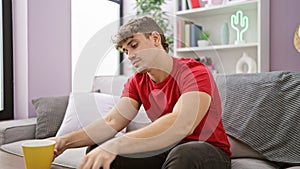 Relaxed morning with a cup of coffee, portrait of a young hispanic man comfortably sitting on his living room sofa at home