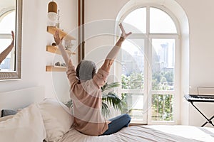 Relaxed older mature woman enjoying being in cozy home bedroom