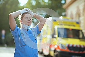 Relaxed paramedic woman breathing outdoors near ambulance