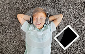 Relaxed preteen boy listening to music on pad, using headset
