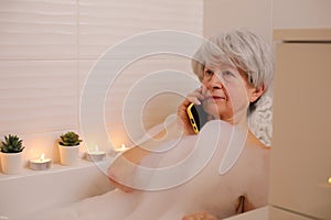 Relaxed senior woman making a phone call in the bathtub