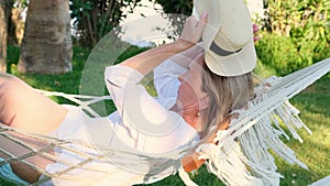 relaxed senior woman in straw hat smiling happy relaxing on a hammock enjoying the fresh air on the terrace around the