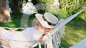 relaxed senior woman in straw hat smiling happy relaxing on a hammock enjoying the fresh air on the terrace around the