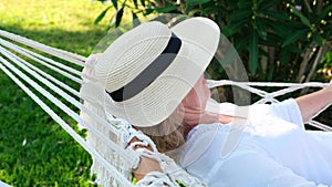 Relaxed senior woman in straw hat smiling happy relaxing on a hammock enjoying the fresh air on the terrace around the