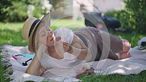 Relaxed senior woman tasting delicious strawberry in slow motion lying on blanket on sunny backyard. Portrait of happy