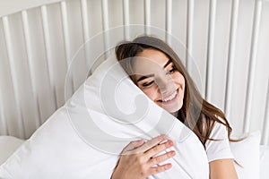 Relaxed sensual happy young woman sitting on bed and hugging pillow at home