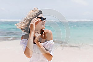 Relaxed short-haired woman posing on sea background. Outdoor shot of blithesome young lady in sunglasses enjoying