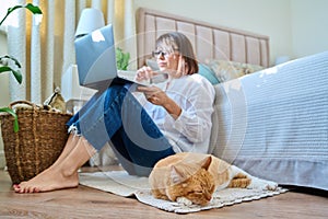 Relaxed sleeping red cat lying on floor, woman with laptop in out of focus