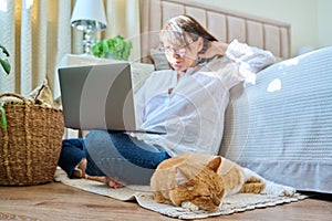 Relaxed sleeping red cat lying on floor, woman with laptop in out of focus