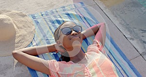 Relaxed, smiling african american woman in sunglasses sunbathing on towel by pool, in slow motion