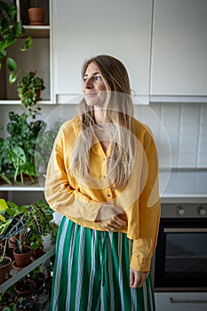 Relaxed smiling relaxed woman standing near home garden on kitchen looking at window daydreaming.