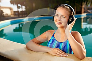 Relaxed smiling woman listening to music in headphones bathing in swimming pool. Blonde girl enjoys favourite song with
