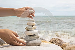 Relaxed spiritually woman hand arrangement pebble tower cobblestone sea coastline landscape closeup photo