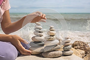 Relaxed spiritually woman hand arrangement pebble tower cobblestone sea coastline landscape closeup photo