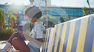 Relaxed student reading book sitting bench sunny street. African girl learning