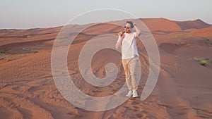 Relaxed tourist man admiring sunset walking in sand dunes in red desert in UAE.