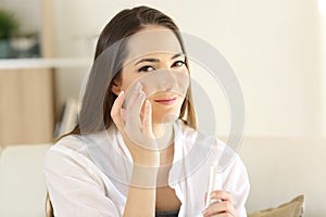 Relaxed woman applying moisturizer cream in cheek