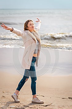 Relaxed woman, arms rised, enjoying spring sun, on a beautiful beach. Young lady feeling free, relaxed and happy