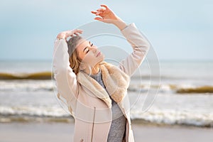 Relaxed woman, arms rised, enjoying spring sun, on a beautiful beach. Young lady feeling free, relaxed and happy