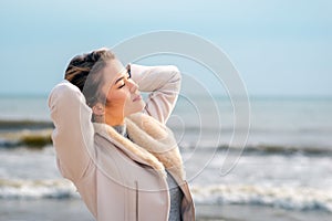 Relaxed woman, arms rised, enjoying spring sun, on a beautiful beach. Young lady feeling free, relaxed and happy