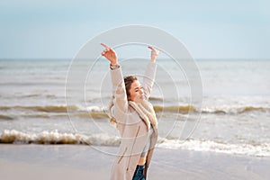 Relaxed woman, arms rised, enjoying spring sun, on a beautiful beach. Young lady feeling free, relaxed and happy
